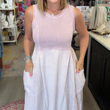 A woman wearing a sleeveless two-tone dress with a light pink bodice and a white skirt with side pockets, standing inside a retail boutique.