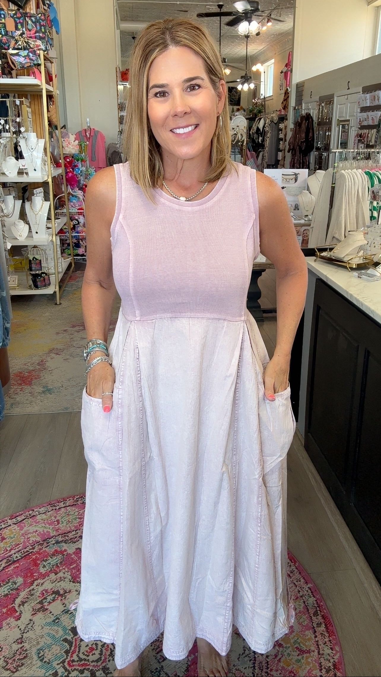 A woman wearing a sleeveless two-tone dress with a light pink bodice and a white skirt with side pockets, standing inside a retail boutique.