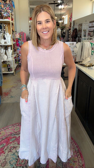 A woman wearing a sleeveless two-tone dress with a light pink bodice and a white skirt with side pockets, standing inside a retail boutique.