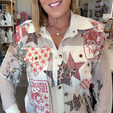 A smiling woman wearing a long-sleeve button-up shirt with a patchwork print featuring red, beige, brown, and white patterns, paired with blue jeans in what appears to be a retail store.