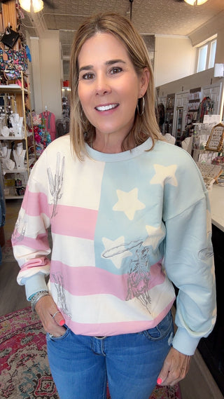 A woman wearing a light blue, pink, and white sweatshirt with a western-themed graphic print, paired with blue jeans, standing inside a retail store.