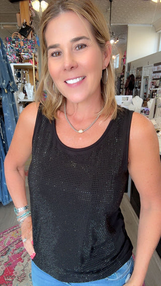 A woman wearing a black sequined sleeveless tank top and blue jeans, standing inside a retail store.