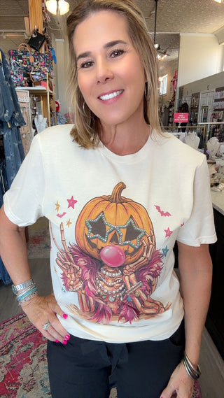 A woman wearing a cream-colored graphic t-shirt with a Halloween-themed pumpkin illustration, standing inside a retail store.