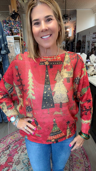A woman wearing a festive red long-sleeve sweater with a Christmas tree pattern, paired with blue jeans, standing in a retail store.