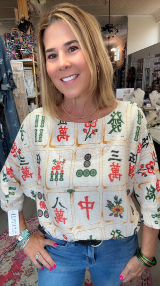 A woman wearing a short-sleeve top with a Mahjong tile pattern, standing in a retail store.