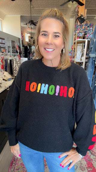 A woman wearing a black crewneck sweater with the word 'OHIOHIOH' spelled out in colorful letters across the chest, paired with blue jeans, standing inside a retail store.
