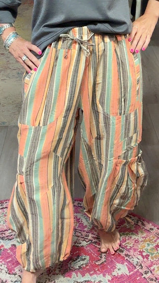 A woman modeling a dark gray long-sleeve top and orange, green, and beige striped cargo pants inside a boutique.