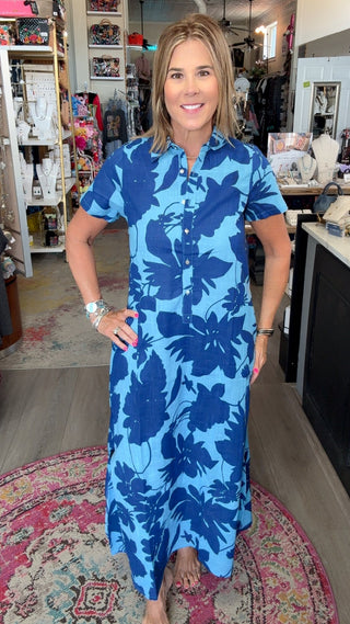 A woman wearing a blue and light blue floral print short-sleeve button-down dress stands inside a retail store.
