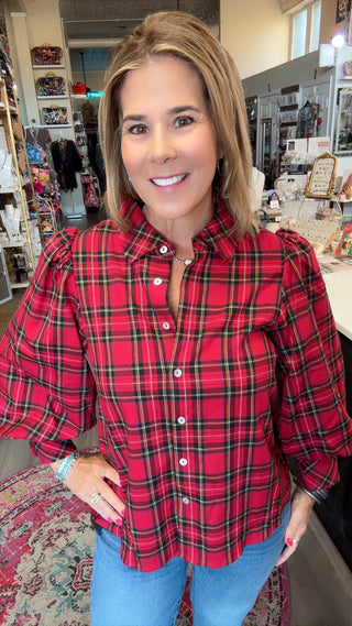 A woman wearing a red and black plaid button-down shirt with puff sleeves, standing in a retail store.