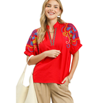 Woman wearing a red embroidered blouse with colorful designs on a white background