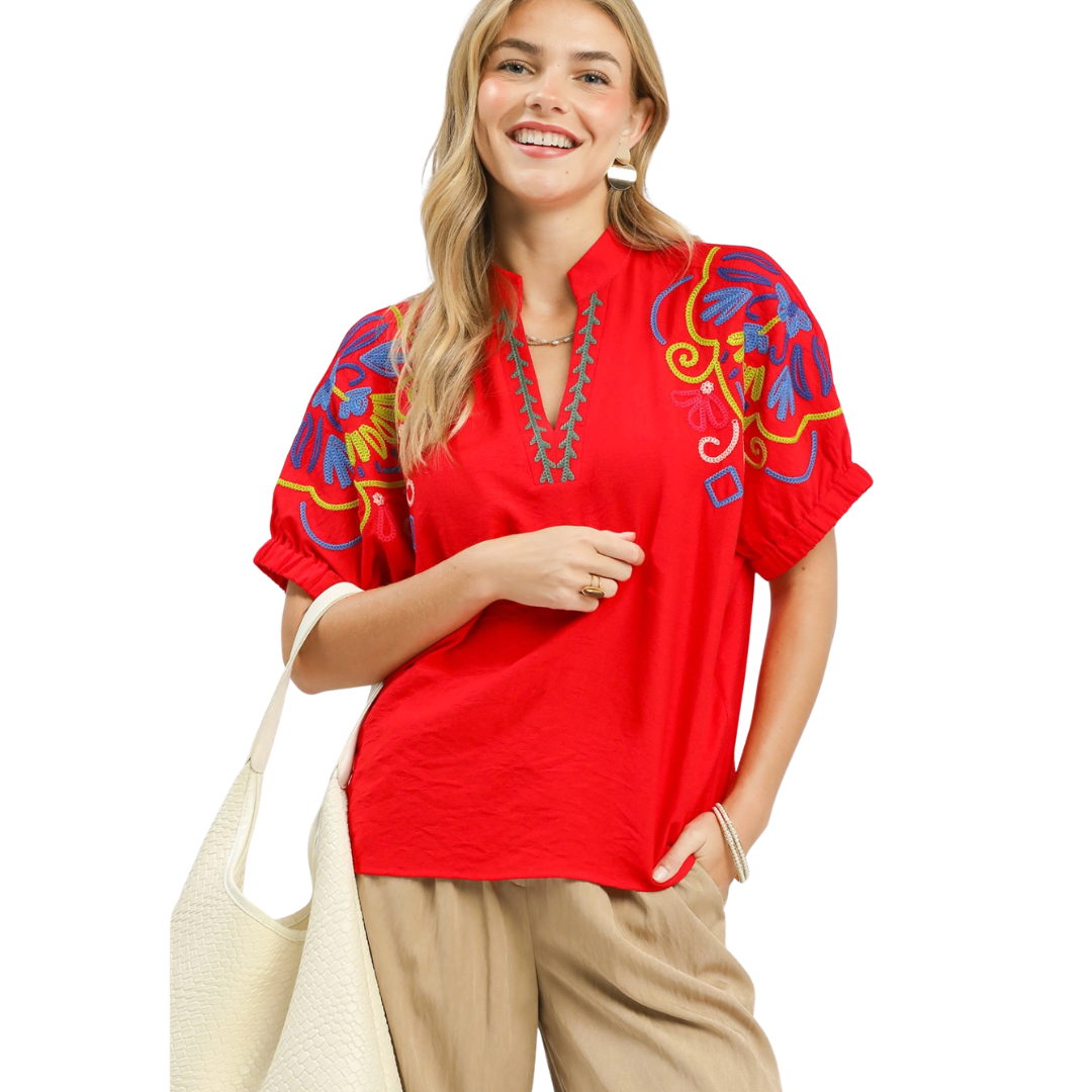 Woman wearing a red embroidered blouse with colorful designs on a white background