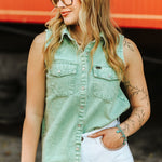 Woman wearing a green sleeveless denim shirt and white pants against an orange background