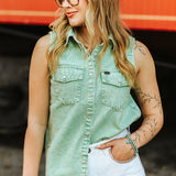 Woman wearing a green sleeveless denim shirt and white pants against an orange background