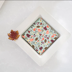 Small square of chocolate with a floral pattern on a white plate, surrounded by autumn-themed decorations.