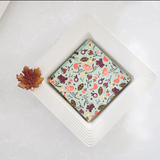 Small square of chocolate with a floral pattern on a white plate, surrounded by autumn-themed decorations.