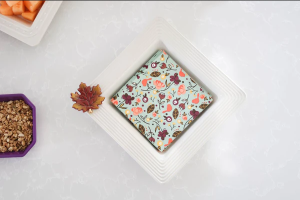 Small square of chocolate with a floral pattern on a white plate, surrounded by autumn-themed decorations.