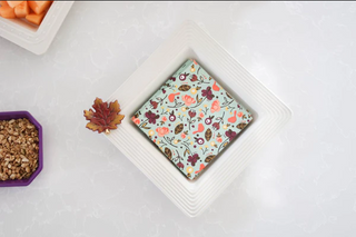 Small square of chocolate with a floral pattern on a white plate, surrounded by autumn-themed decorations.