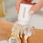 Hand holding a Shinery product near a wrist with a gold watch and white lace bracelet.