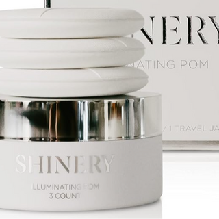Skincare product jar labeled 'SHINERY' with a blurred magazine in the background