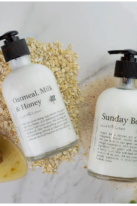 Two bottles of skincare products labeled 'Oatmeal, Milk & Honey' and 'Sunday Body' on a textured surface.