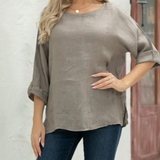 Woman wearing a gray blouse and blue jeans standing against a white wall.