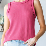 Woman wearing a pink sleeveless top and light blue jeans with a decorative wreath in the background.