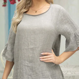 A woman wearing a gray linen top with bell sleeves and blue jeans.