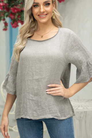 A woman wearing a gray linen top with bell sleeves and blue jeans.