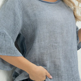 A woman wearing a blue linen top with bell sleeves, paired with jeans.