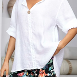 Woman wearing a white shirt and colorful floral pants in a minimalistic setting.