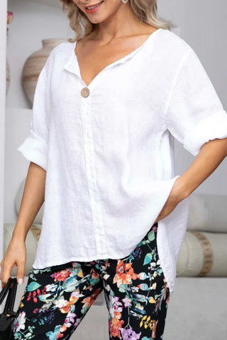 Woman wearing a white shirt and colorful floral pants in a minimalistic setting.