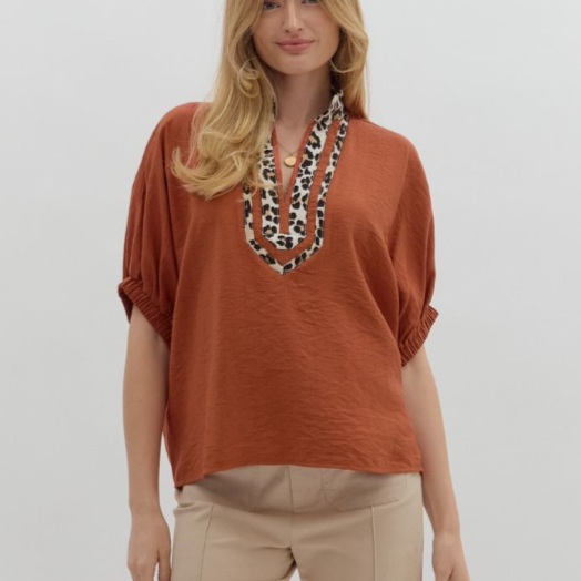 Woman wearing a rust-colored top with a leopard print necklace on a plain background