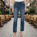 Person wearing blue jeans standing on a street with outdoor seating in the background