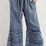 Blue denim pants with ruffled bottom hem on a white background