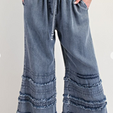 Blue denim pants with ruffled bottom hem on a white background
