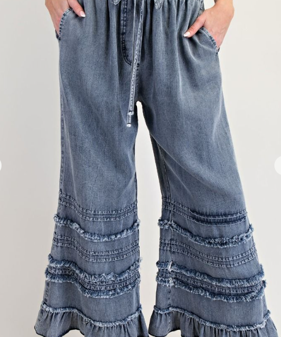 Blue denim pants with ruffled bottom hem on a white background