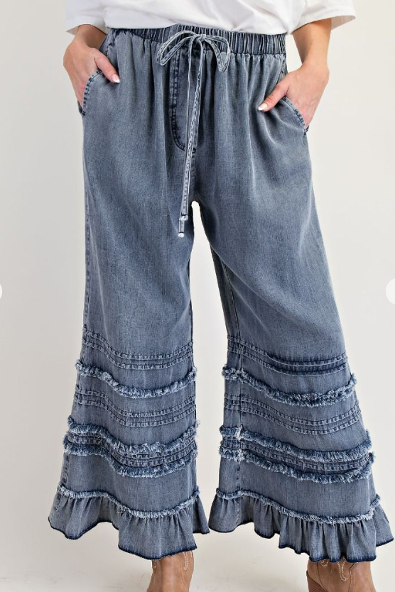 Blue denim pants with ruffled bottom hem on a white background
