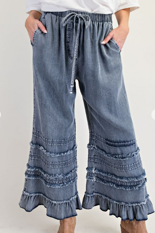 Blue denim pants with ruffled bottom hem on a white background