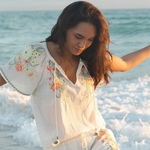 Woman in a floral dress standing on a beach with ocean waves in the background