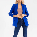 Woman wearing a blue blazer over a beige top and blue jeans on a white background
