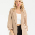 Woman wearing a beige blazer over a white top and black pants on a white background