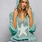 Woman wearing a teal crochet hoodie against a gray background
