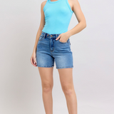 Woman wearing a light blue sleeveless top and denim shorts on a white background