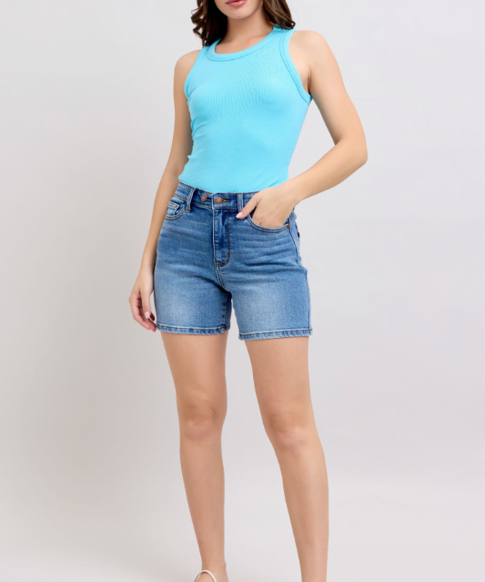 Woman wearing a light blue sleeveless top and denim shorts on a white background