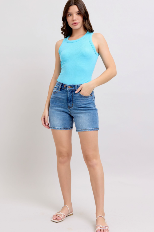 Woman wearing a light blue sleeveless top and denim shorts on a white background