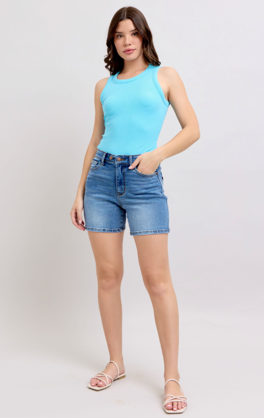 Woman wearing a light blue sleeveless top and denim shorts on a white background