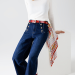 Woman wearing a white turtleneck, blue jeans, red belt, and beige cap on a white background