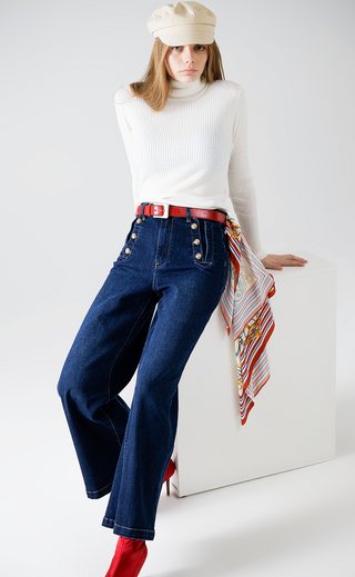 Woman wearing a white turtleneck, blue jeans, red belt, and beige cap on a white background
