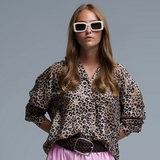 Woman wearing a leopard print blouse and pink pants with white sunglasses on a gray background