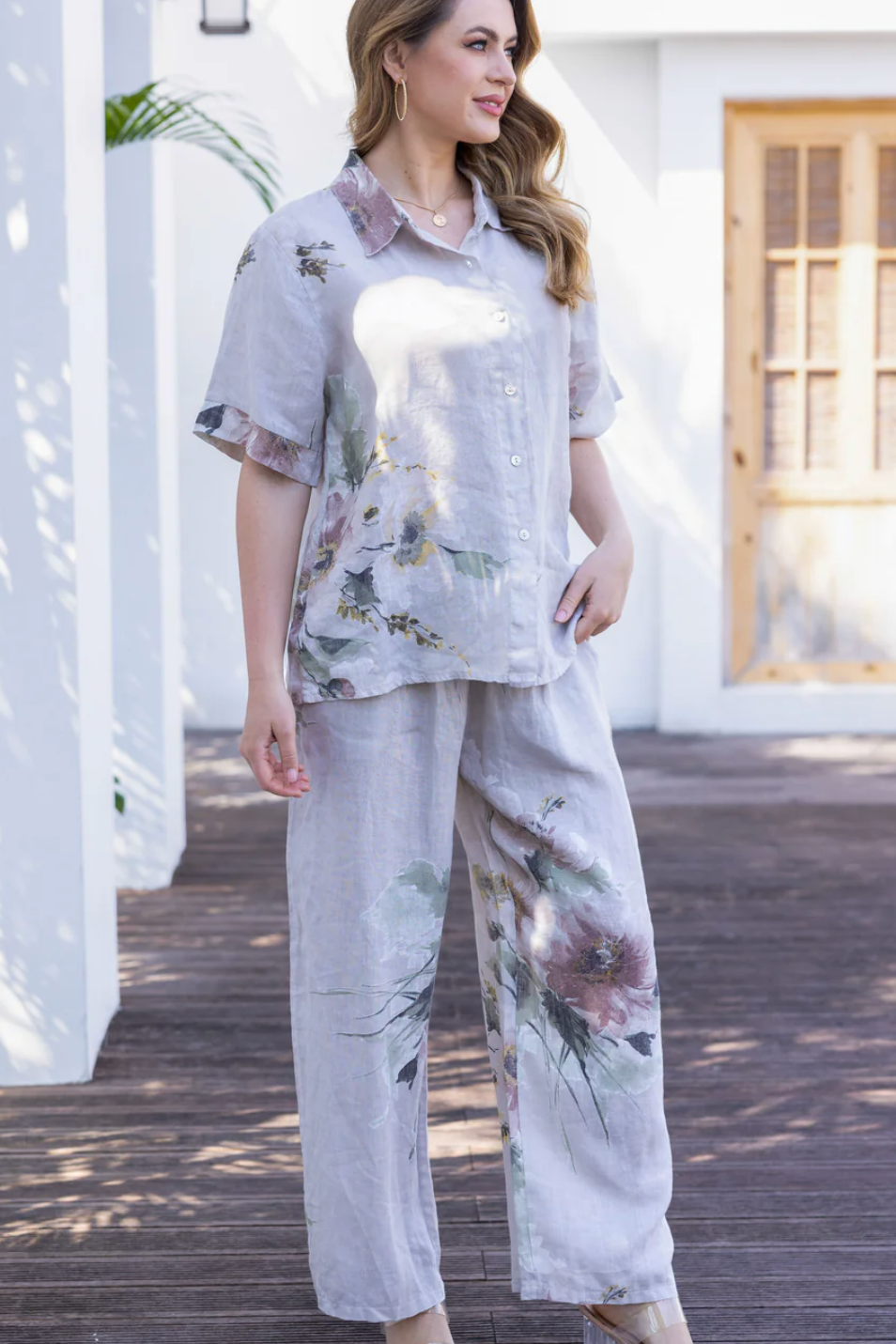 Woman wearing a floral outfit standing on a wooden deck.